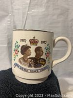 The front side of the Queen's Silver Jubilee mug showing Queen Elizabeth and Prince Philip, the crown, and years 1952 and 1977 with floral decoration.
