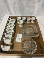 Overview photo showing 8 white ceramic dove napkin ring holders, 4 ceramic egg cups with floral and solid designs, and 2 clear heavy crystal bowls in a cardboard box.