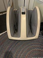 Front view of the vintage leg massager showing the off-white plastic frame and two grey fabric compartments for legs and feet.