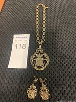 Photo showing full necklace with pendant and pair of matching screw-back earrings placed on dark textured background with auction lot card