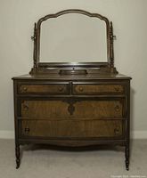 Front view of antique wooden dresser with four drawers and an ornate framed mirror attached on top.