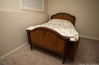 Photo of antique double bed showing wooden frame with curved headboard and footboard in room corner.