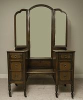 Front view of dark wood antique makeup dresser with tri-fold mirror panels and six drawers.