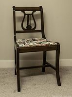 Front view of antique wooden makeup table chair with carved lyre design back and floral upholstered seat.