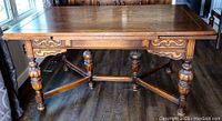 Front view of rectangular oak dining table showing carved aprons, turned legs, and X-shaped stretcher.
