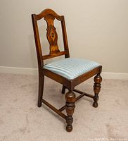 Single antique wooden dining chair with carved backrest and blue/white striped upholstered seat, front angled view.