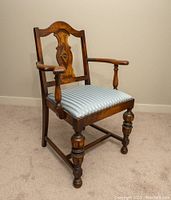 Image showing one antique wooden dining room chair with carved backrest, turned legs, armrests, and blue and white striped upholstered seat.
