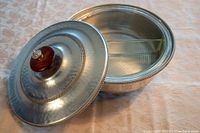 Oval metal serving dish with lid featuring wooden knob handle, decorative beaded rim, and internal divider.
