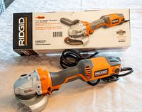 Ridgid 4 1/2 inch angle grinder placed on a table alongside the original box showing product image and branding.