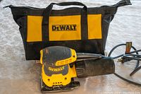 Photo of Dewalt corded 1/4 sheet palm sander with dust collection box and black-and-yellow Dewalt carrying bag.