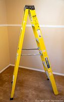 Photo of yellow 6 foot Industrial Lite step ladder with black top and metal braces, placed indoors on carpeted floor.
