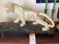 Side view of tiger statue showing detailed snarling face and tail curved back, with orange and cream veining visible in the stone.