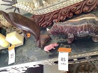 Set of three animal sculptures displayed on a tabletop, showing wooden dolphin, stone rhinoceros, and pink stone hippo.