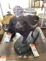 Front three-quarter view of bronze ram sculpture on glass-topped table showing head and horn detail