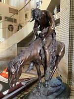 Front view of bronze rider slumped on horse atop oval base with staircase background
