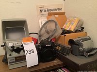 Overview of lot: Baia film editor/viewer, Nikon D7100 DSLR, Canon camcorder, SanDisk card and manuals