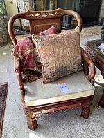 Carved wooden chair with beige seat cushion and two decorative throw pillows.