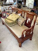 Carved wooden sofa with white bench cushion and multiple decorative throw cushions arranged on top. Sofa has intricate white floral inlays on the backrest and arm rests.