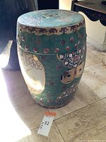 Photo of decorative ceramic stand showing side details with floral and bird designs, turquoise green with gold and red accents