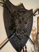 Metal coat of arms showing embossed eagle, crossed swords, and spiked mace