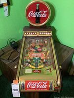 Front view of entire tabletop pinball machine with illuminated Coca-Cola bottle sign on top.