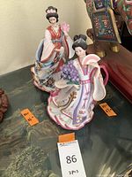 Two Danbury Mint geisha lady sculptures displayed on a surface, showing the detailed colorful kimonos and floral patterns.
