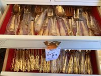 Two-drawer view showing assorted gold-tone flatware pieces in protective sleeves