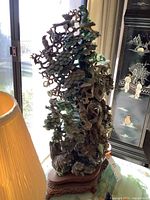 Front three-quarter view of carved jade tree sculpture with multiple birds and foliage, seated on carved wooden stand.