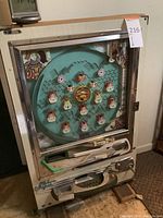Front-facing view of full pachinko machine showing teal playfield, chrome trim, wood sides