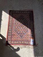 Top view of the entire small Persian rug with shadow partly covering it, showing the overall design and fringed edges.