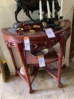 Side view of semi-circular wooden table with marble top showing detailed carving, three tier triangular shelves, and curved legs