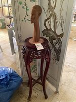 Full image showing the tall wooden pillar table with marble top and wooden African sculpture on top against a decorated folding screen.