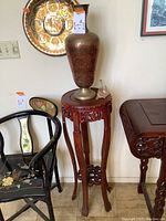 Metal vase on tall carved wooden pillar table, showing side view