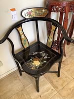Full chair showing black wood with decorative enameled floral panels on the backrest and arms.