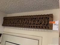 Full view of the carved wooden wall art panel hanging above a door frame showing overall size and design.