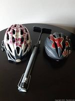 Side view of two bicycle helmets and manual air pump on black table