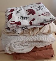 Top sheet with white base and red and black plaid moose and tree pattern is a Canadiana twin flannel sheet. Below are neutral color fitted sheets.