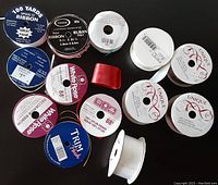 Various unopened and partially used ribbon spools arranged on a black surface showing brands and spool sizes.