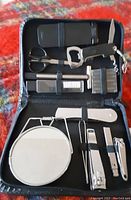 Open black leather zippered case showing contents of the men's grooming and manicure set laid out inside, including scissors, mirror, razor, bottle opener, and other tools