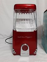 Front view of Nostalgia hot air popcorn maker in shiny red with transparent popcorn chamber and power cord.