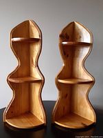 Pair of solid wood corner shelves with a sculptural organic shape and three shelving surfaces each, standing upright side by side.