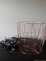 Rose gold wireframe metal basket next to coiled string of lights with clear bulbs on black wire