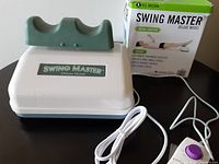 White and green Swing Master aerobic exerciser device with ankle cradle on top and original packaging box in background.