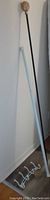 Shows full length of the white tension rod, black extendable rod with wooden end, and curved white 4-hook hanger on floor leaning against wall.