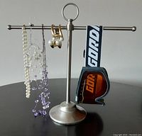 Photo showing the vintage Gordon ski goggles hanging on the right side of a brushed nickel jewelry stand with three custom necklaces and a bracelet hanging on the horizontal bar