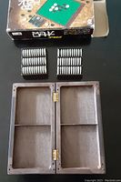 Folded board open inside showing storage compartments and black and white magnetic game pieces in trays, with the original box behind.