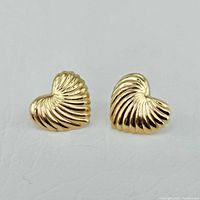 Front view of two ridged heart-shaped gold stud earrings on white background.
