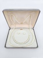 Entire pearl necklace, bracelet and earrings arranged inside open gray velvet box