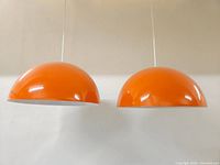 Two orange dome shades hanging side by side from white cords