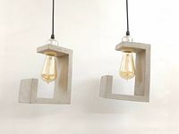 Front view of two pendant lights with concrete 'C' shaped shades and Edison bulbs hanging side by side